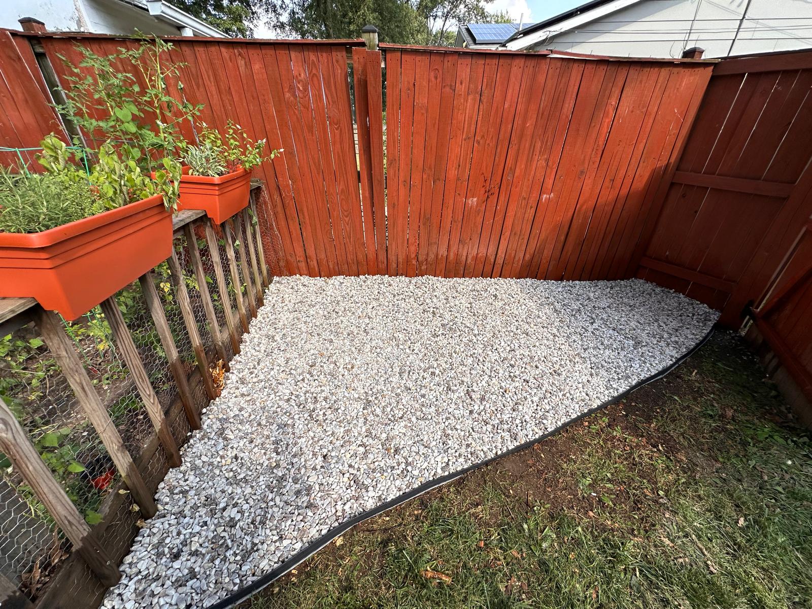 Finished white gravel area with curved black edging beside a fence